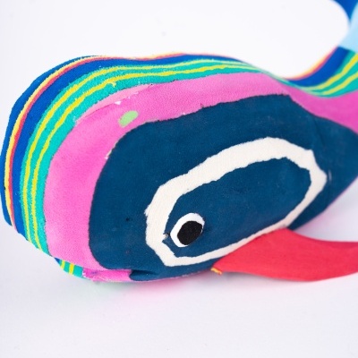 Pelúcia em forma de peixe com listras coloridas e olho desenhado