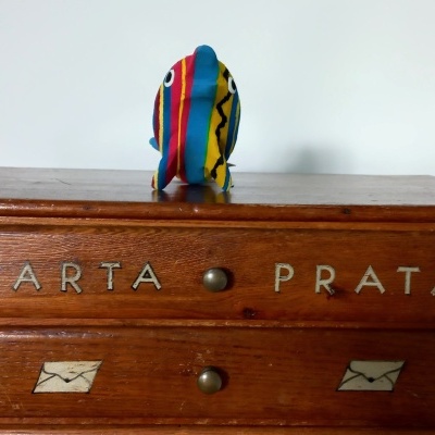 Gaveteiro de madeira castanha com inscrições e figura colorida em tecido no topo