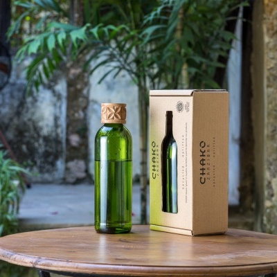 Garrafa de vidro verde com tampa de cortiça e caixa de cartão reciclado sobre mesa redonda de madeira