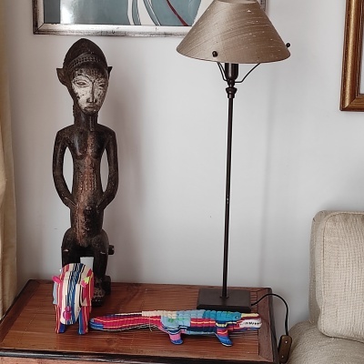 Escultura de madeira humana, candeeiro de pé e esculturas coloridas sobre uma mesa de madeira