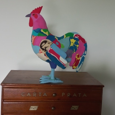 Estatueta colorida de galinha em madeira pintada sobre mesa de madeira.