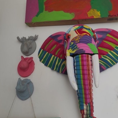 Cabeça de elefante colorida em tecido e três cabeças de animais decorativas numa parede branca