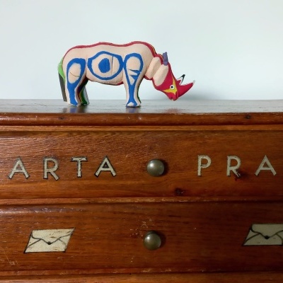 Móvel em madeira com duas gavetas e letras metálicas, com uma escultura de rinoceronte no topo