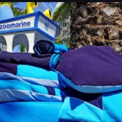 Produtos têxteis azuis e roxos ao ar livre junto a árvore e placa Zoomarine