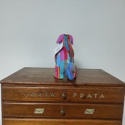 Figura decorativa de cão colorido em tecido sobre móvel em madeira com gavetas