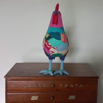 Pássaro decorativo colorido em tecido sobre móvel de madeira com inscrição