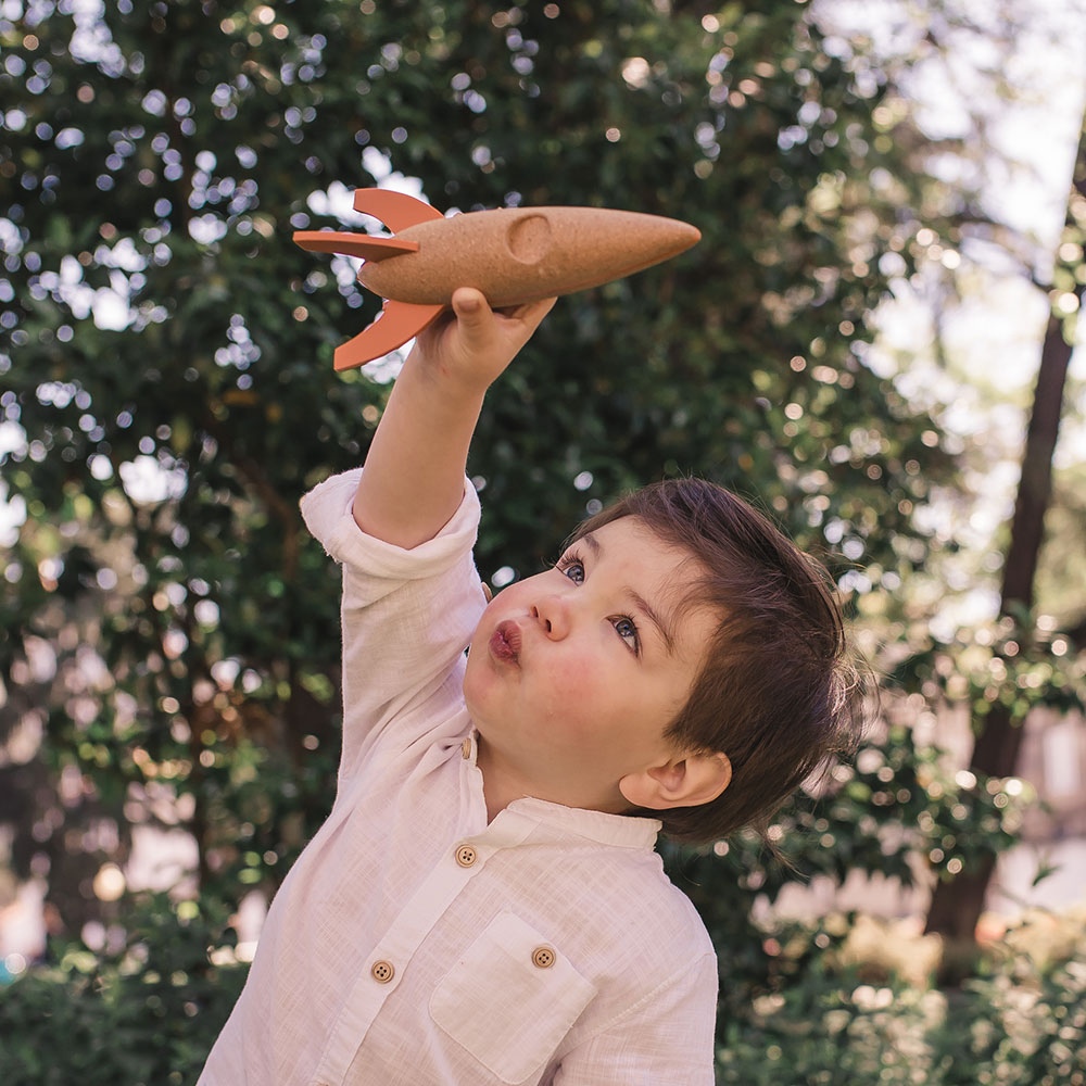 Criança a brincar com foguete de brinquedo castanho e laranja ao ar livre