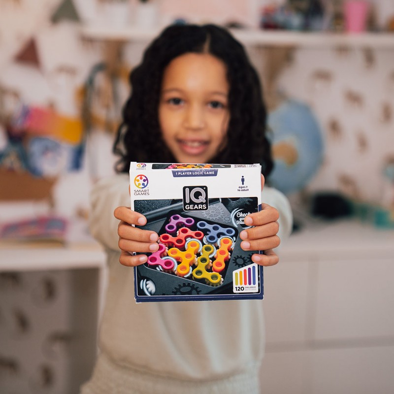 Criança segurando caixa do jogo IQ GEARS de lógica com peças coloridas