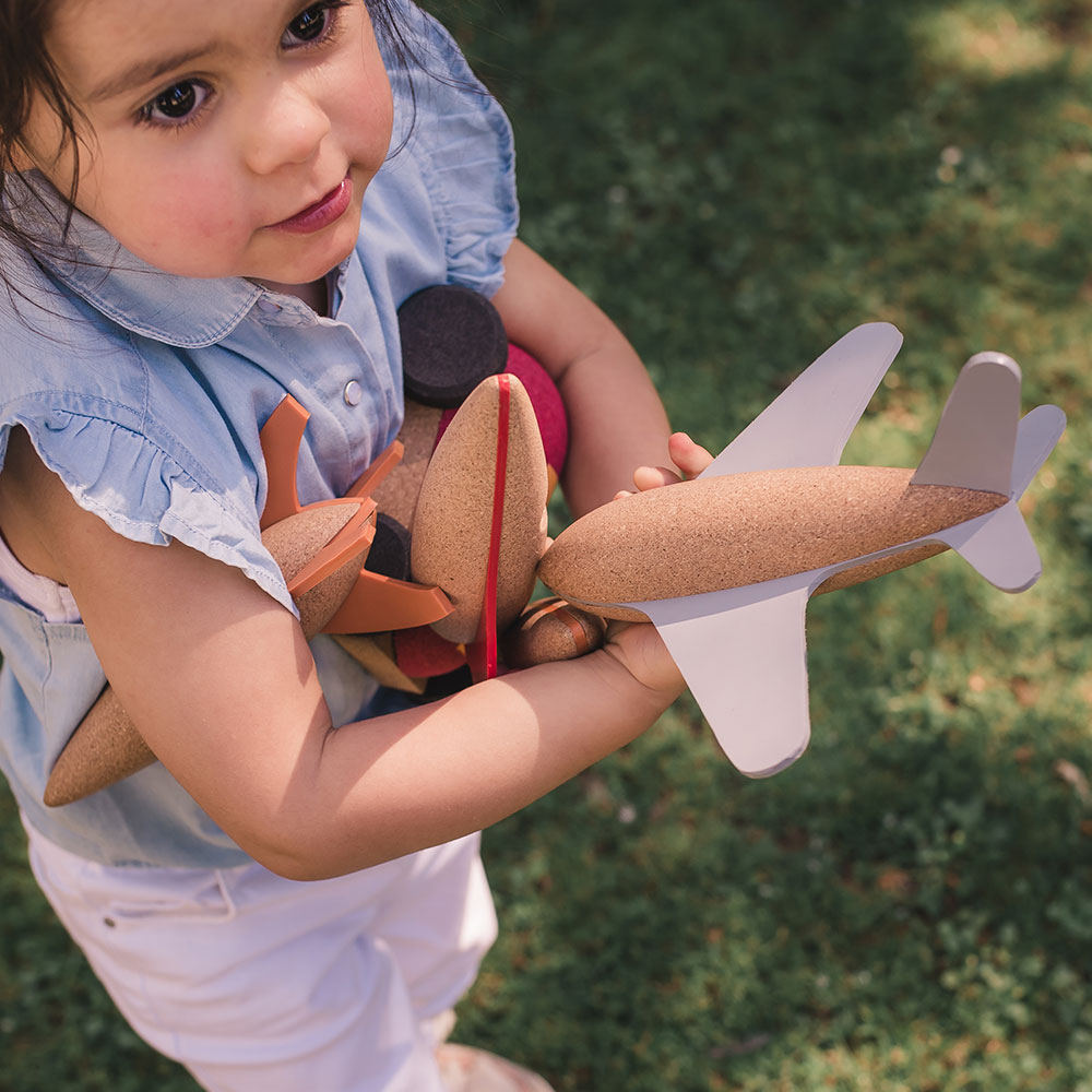 Menina segurando avião de brinquedo feito de cortiça e cinza em relvado