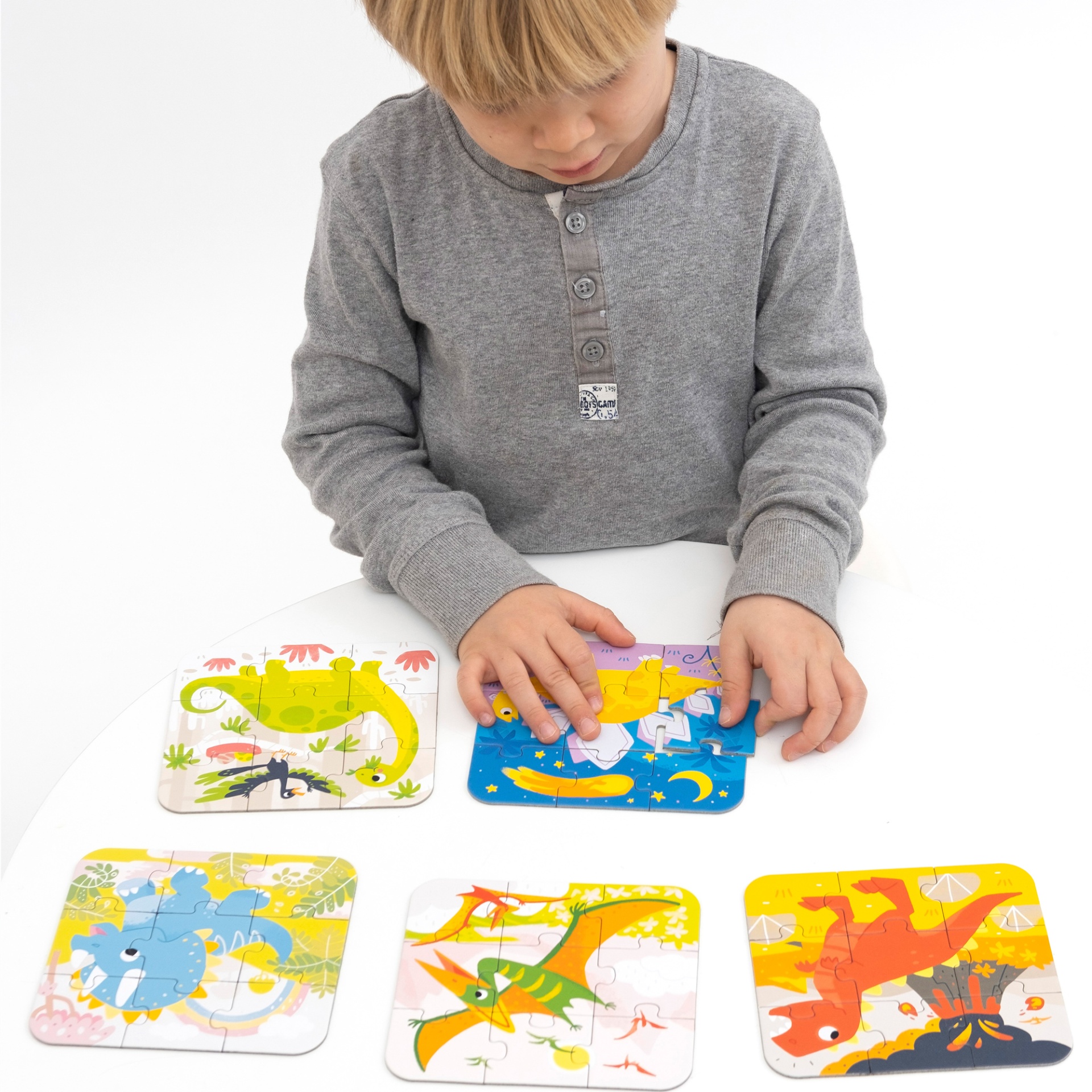 Criança a montar puzzles infantis coloridos com dinossauros e sapo em mesa branca