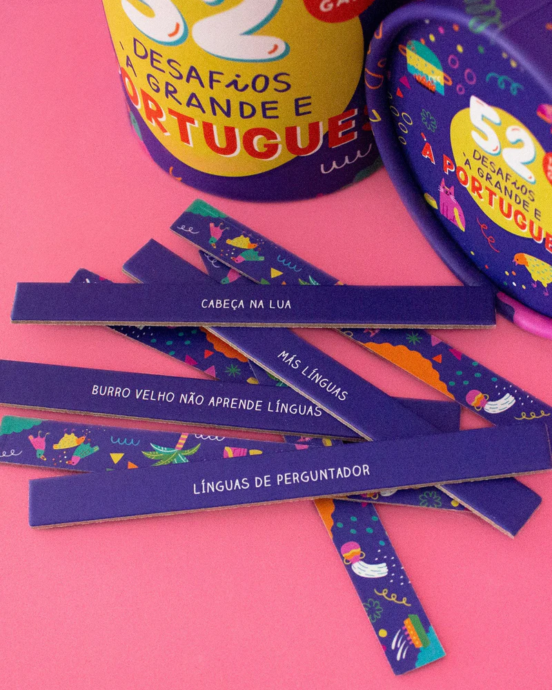 Tiras de cartão coloridas com frases em português e embalagem azul e amarela sobre fundo rosa.