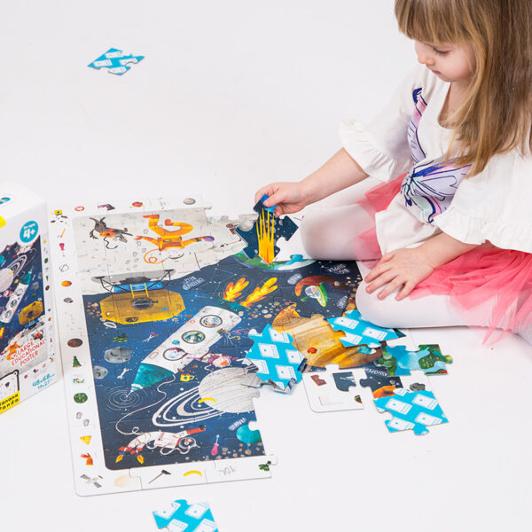Criança a montar puzzle tema espaço com peças coloridas no chão