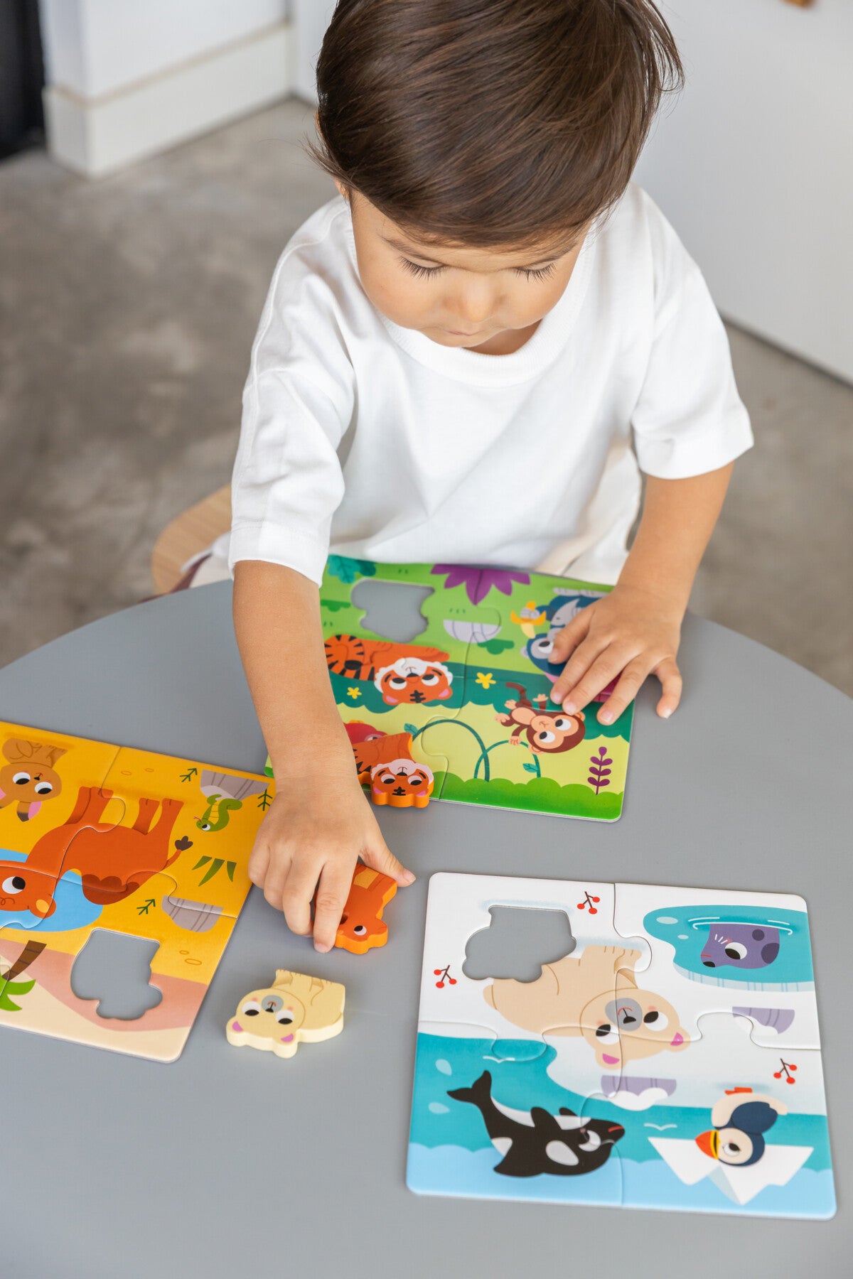 Criança a montar puzzles de animais numa mesa cinza