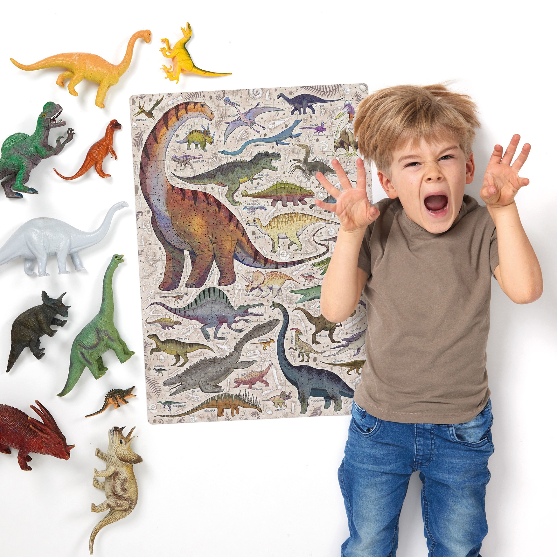 Criança ao lado de dinossauros de brinquedo e tapete ilustrado com dinossauros