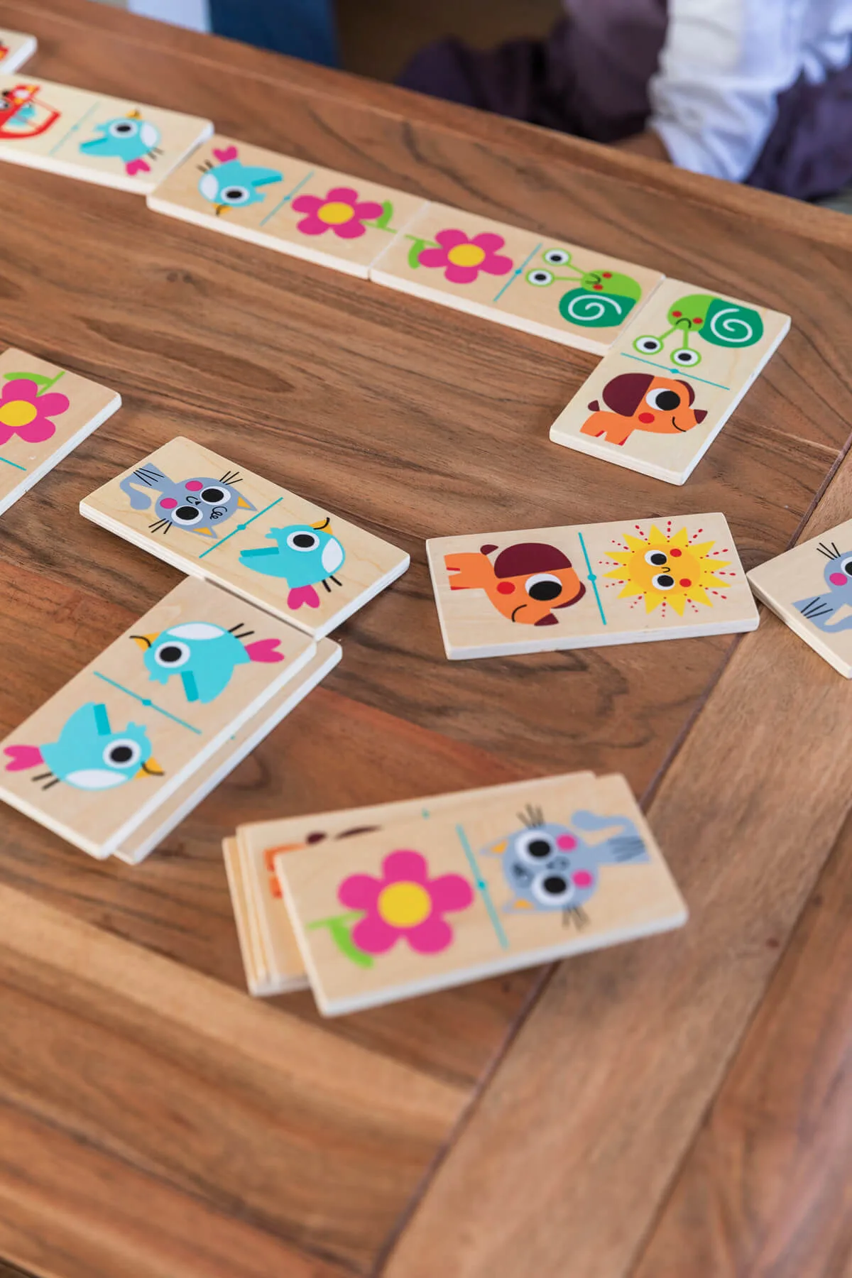 Peças de dominó de madeira com desenhos coloridos de animais e flores espalhadas sobre mesa de madeira