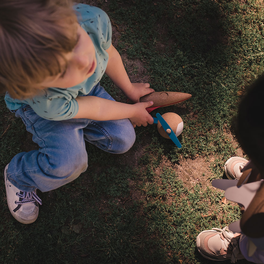 Criança a brincar com avião de brinquedo sentada na relva