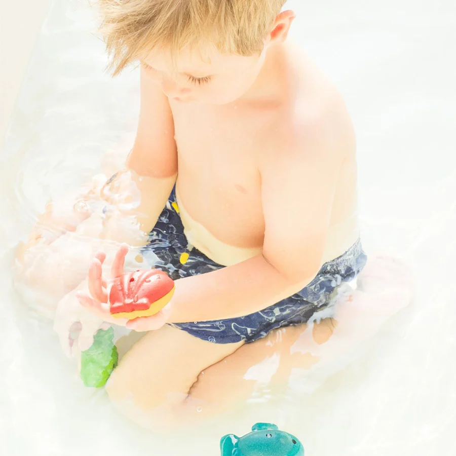 Menino com calções azuis a brincar com brinquedos coloridos na água.
