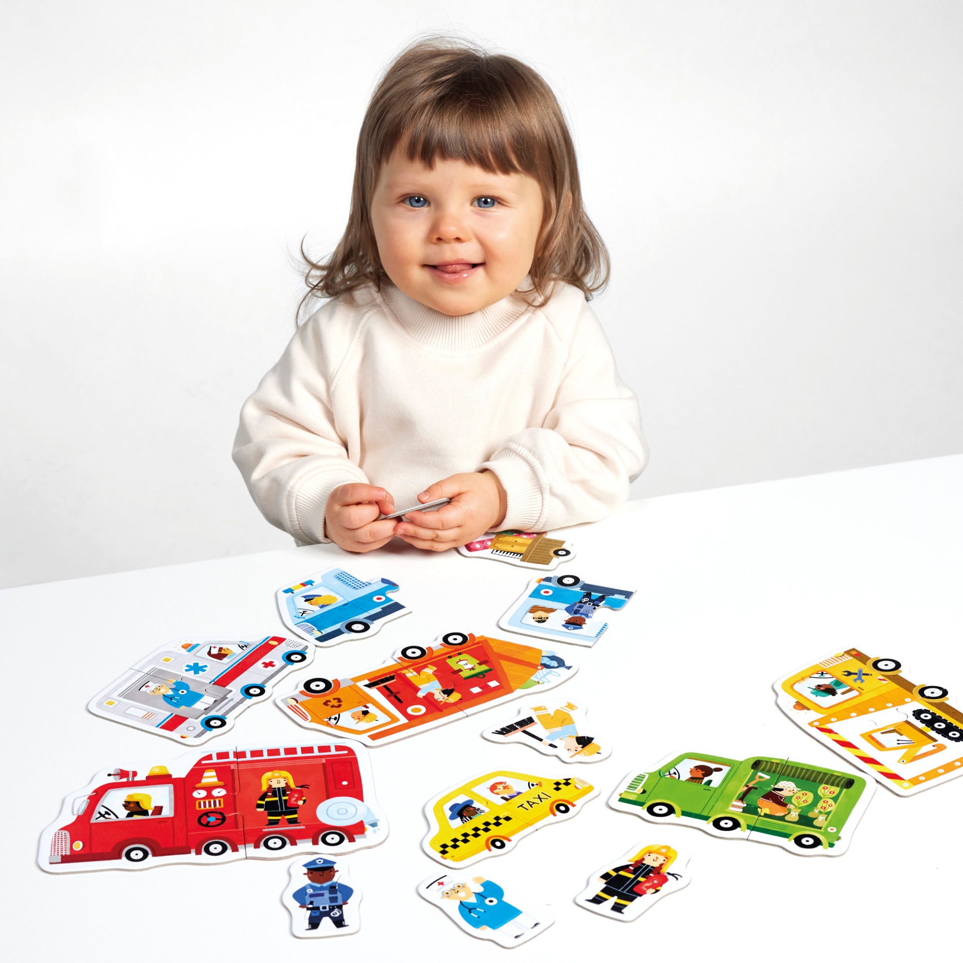 Criança com camisola creme sentada com puzzle de peças grandes de madeira com veículos coloridos