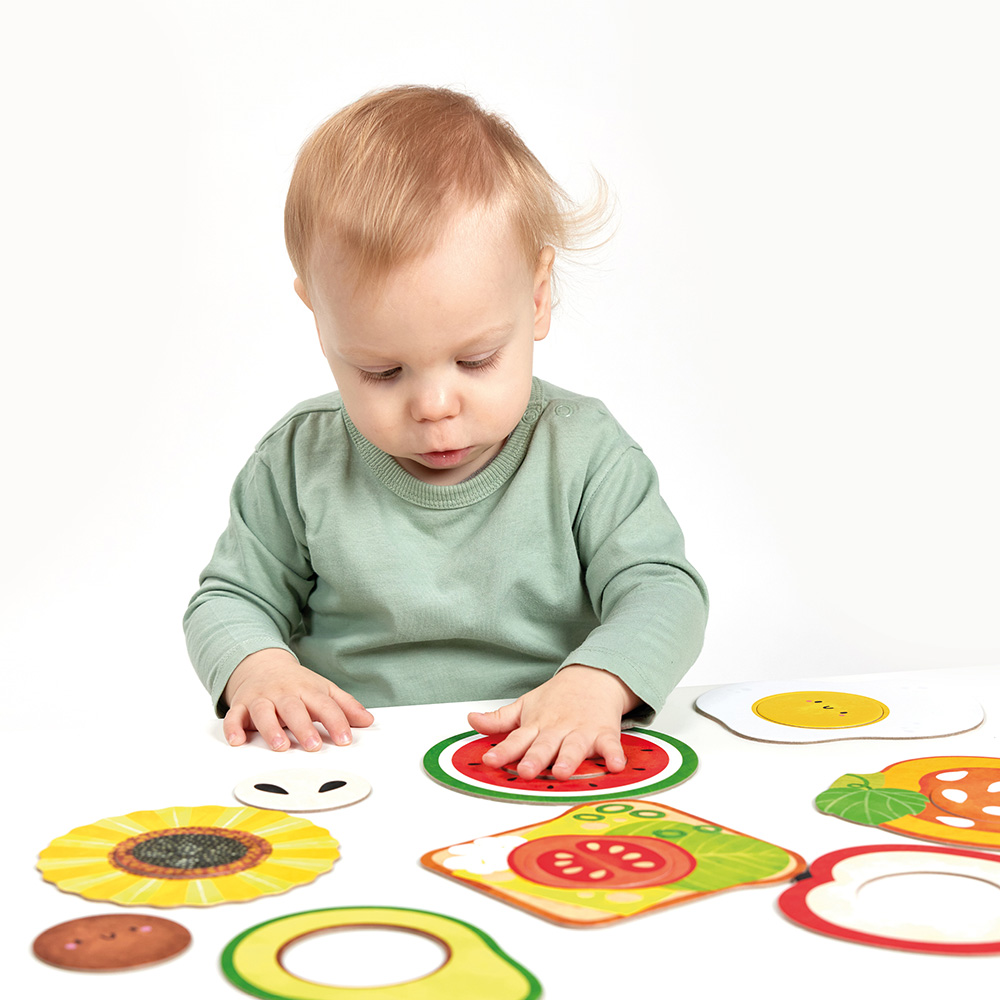 Bebé com camisola verde a jogar com cartas ilustradas de frutas e legumes