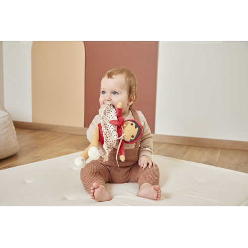 Bebé sentado num colchão branco a mordiscar boneco de pano colorido