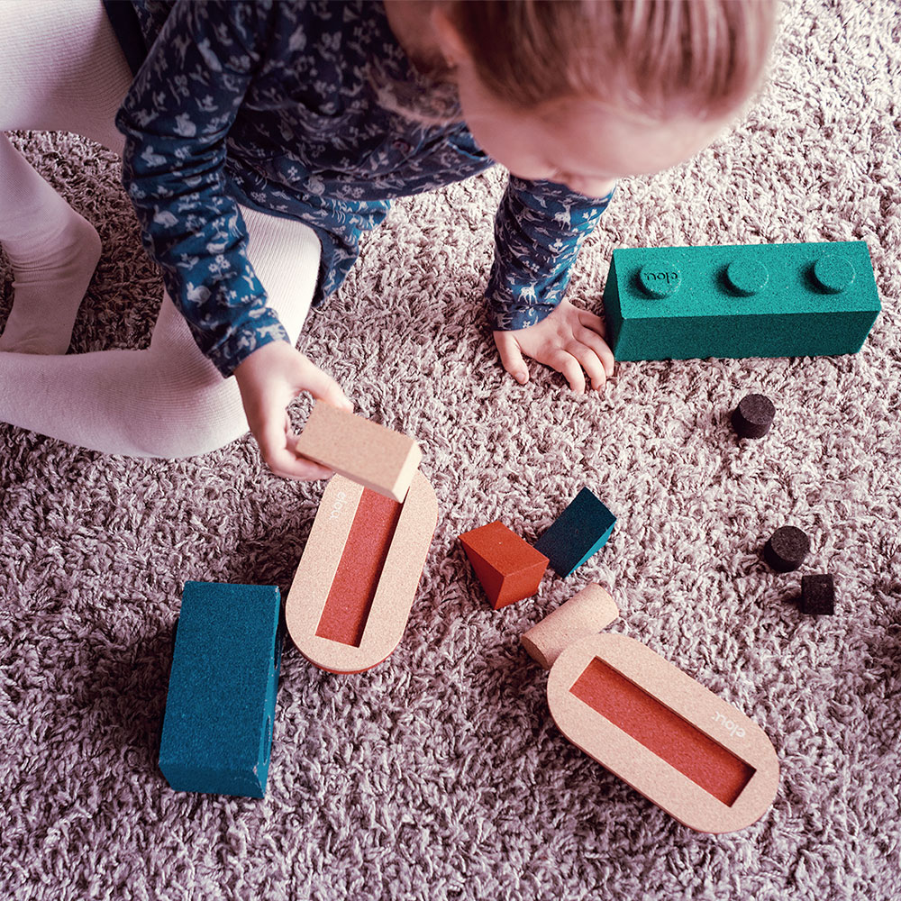 Criança a brincar com blocos de construção de cortiça e espuma sobre carpete cinza