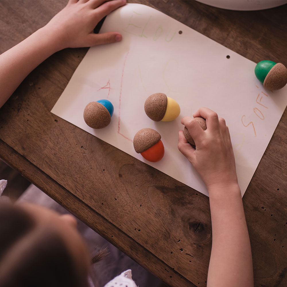 Folha de papel com bolinhas coloridas de madeira e mãos de criança numa mesa de madeira