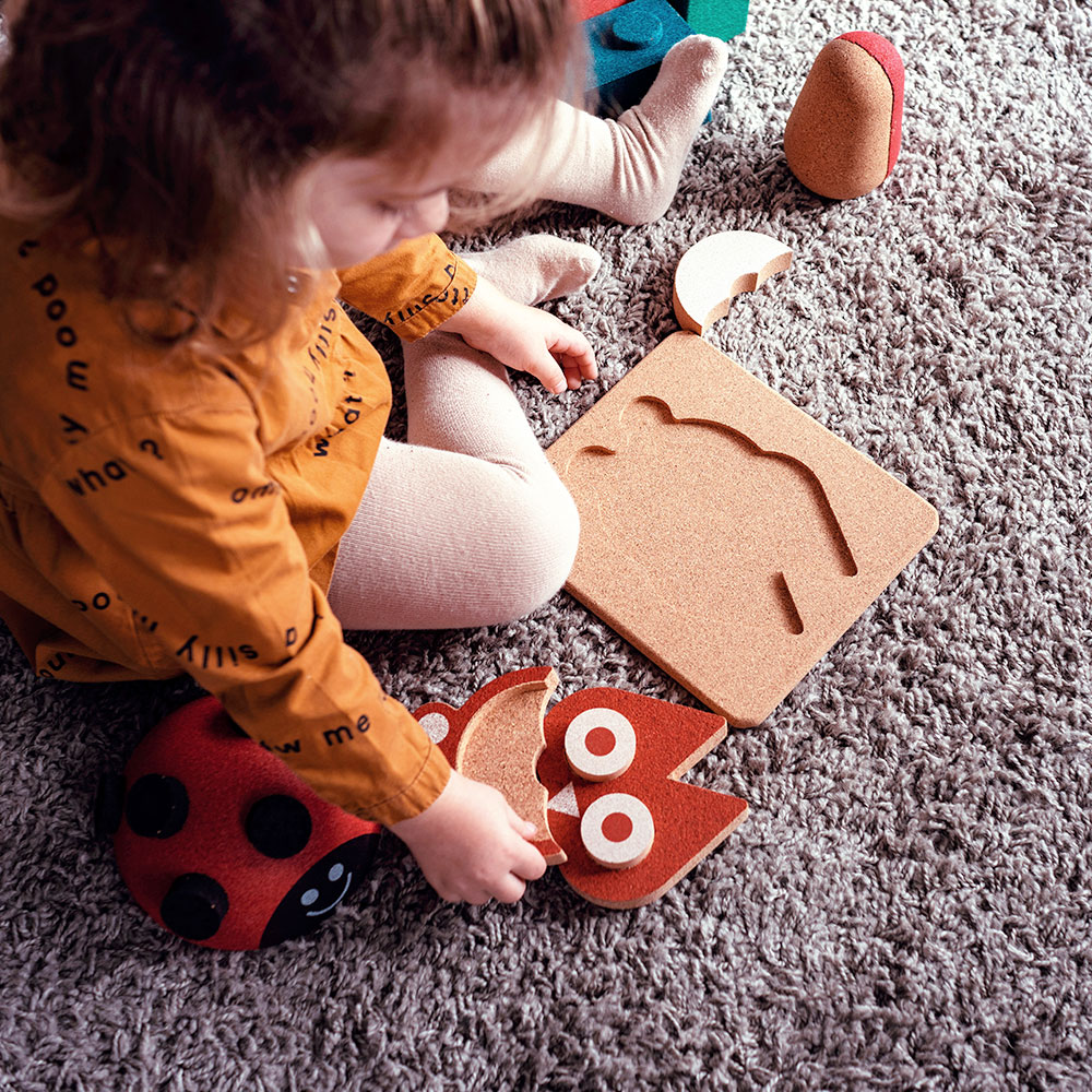 Criança a brincar com brinquedos de madeira e cortiça no tapete cinza