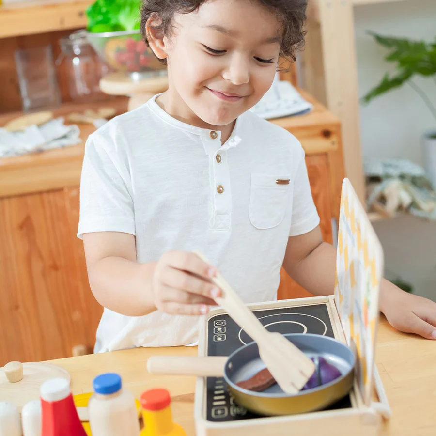 Criança a brincar com brinquedo de cozinha em madeira e utensílios coloridos