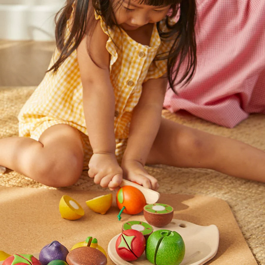 Menina a brincar com brinquedos de frutas de madeira coloridas sentada no chão