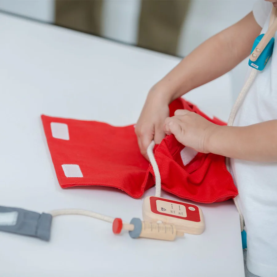Brinquedo de médico em tecido vermelho com acessórios em madeira e criança a usar
