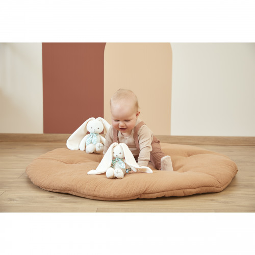 Bebé num tapete almofadado castanho com dois coelhos de peluche brancos