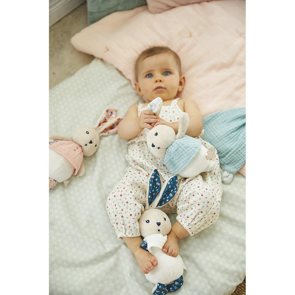 Bebé de macacão branco com padrão colorido e brinquedos de peluche coelho