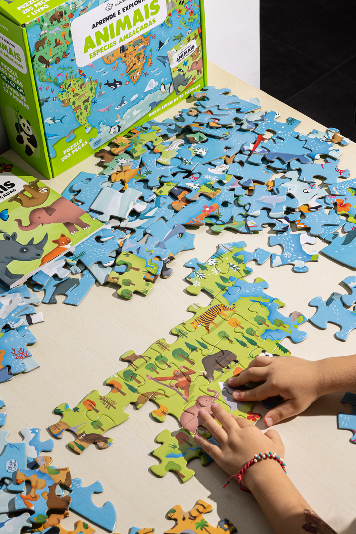 Puzzle educativo sobre animais ameaçados sendo montado sobre uma mesa com caixa verde ao fundo