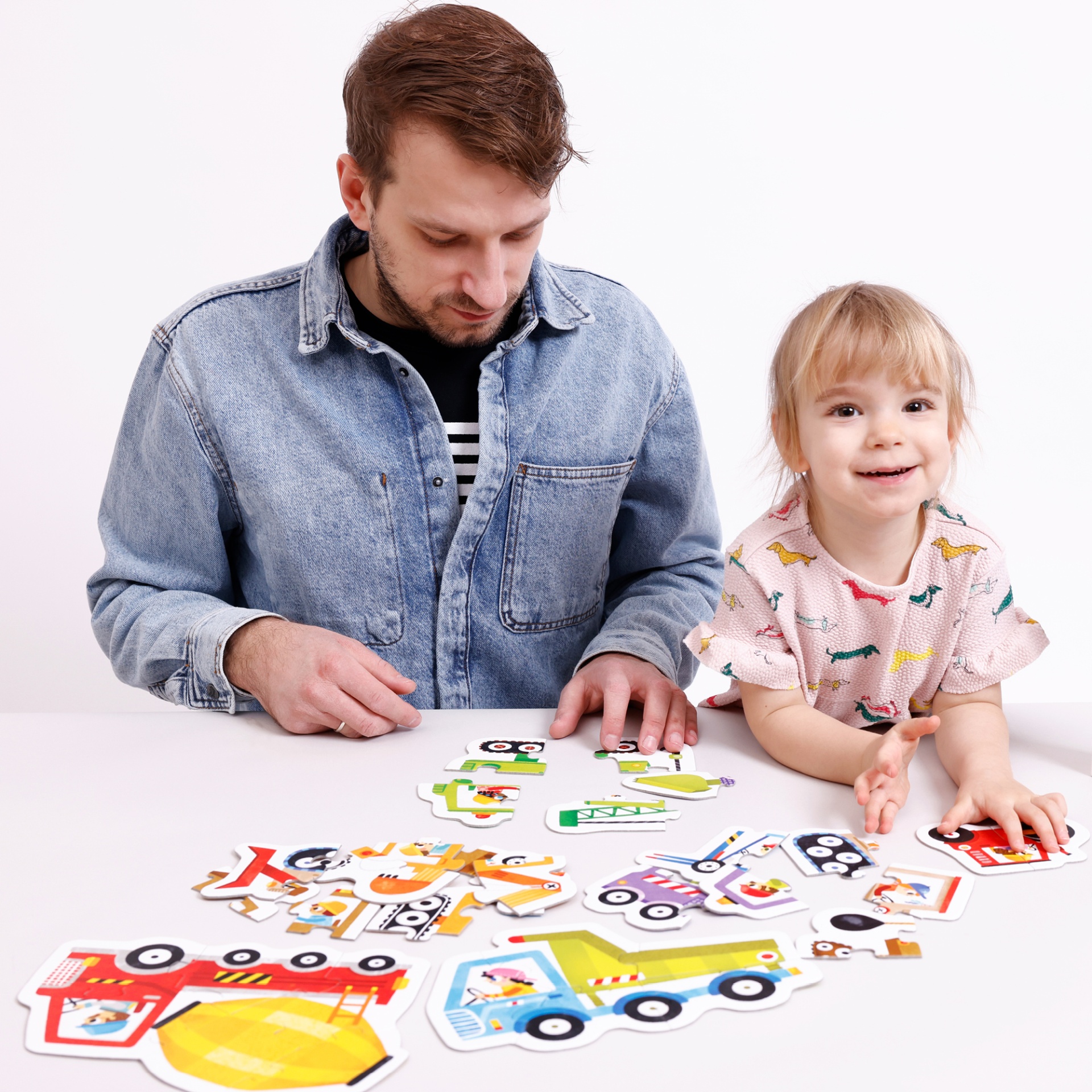 Homem e criança a brincar com puzzles de madeira coloridos numa mesa branca
