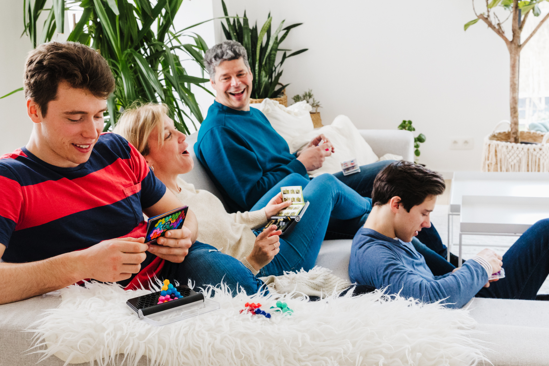 Grupo de pessoas a jogar jogo de tabuleiro em sofá e chão com peças coloridas e cartas