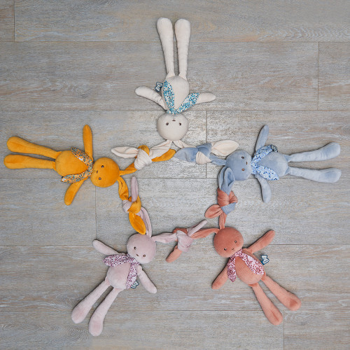 Cinco bonecos de coelho de peluche coloridos dispostos em círculo sobre chão de madeira clara