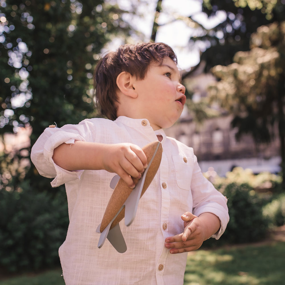 Criança de camisa branca segura avião de brinquedo de madeira ao ar livre
