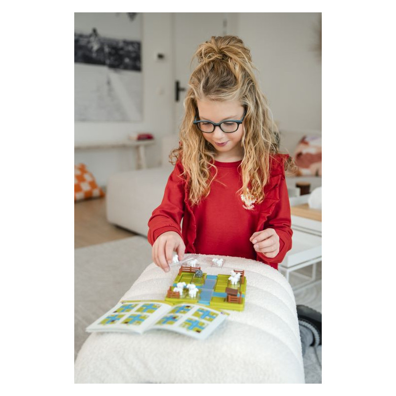 Menina loira de óculos jogando jogo de tabuleiro sobre sofá branco.