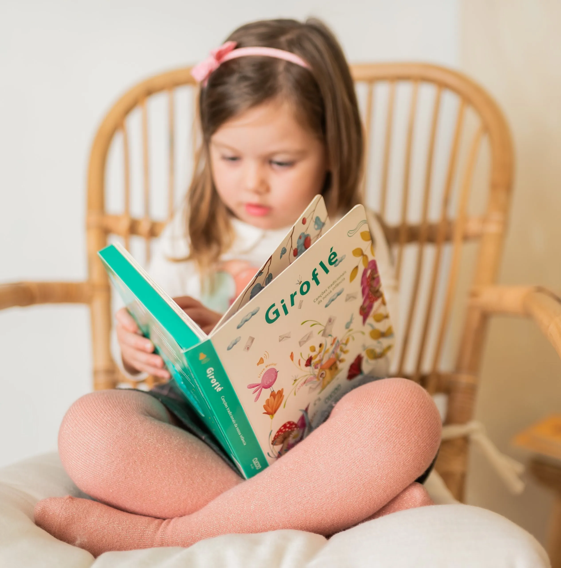 Criança a ler livro Giroflé sentada numa cadeira de vime, collants rosa brilhantes