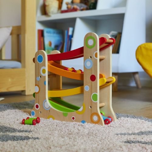 Brinquedo de madeira colorido com rampas e carrinhas num quarto infantil.