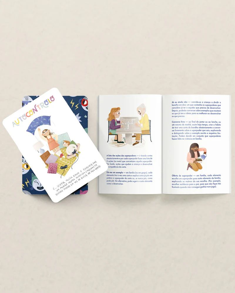 Jogo de cartas e livro aberto com texto e ilustrações sobre mesa clara.