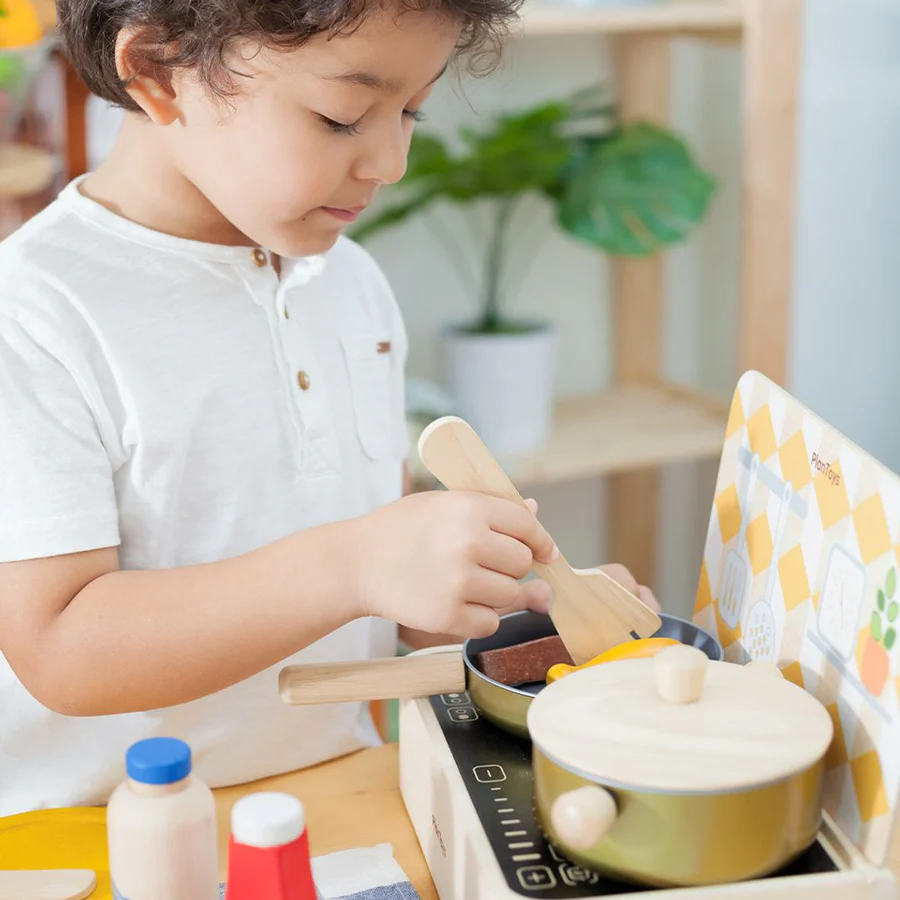 Criança a brincar com conjunto de cozinha de brinquedo de madeira e plástico com panelas douradas e utensílios
