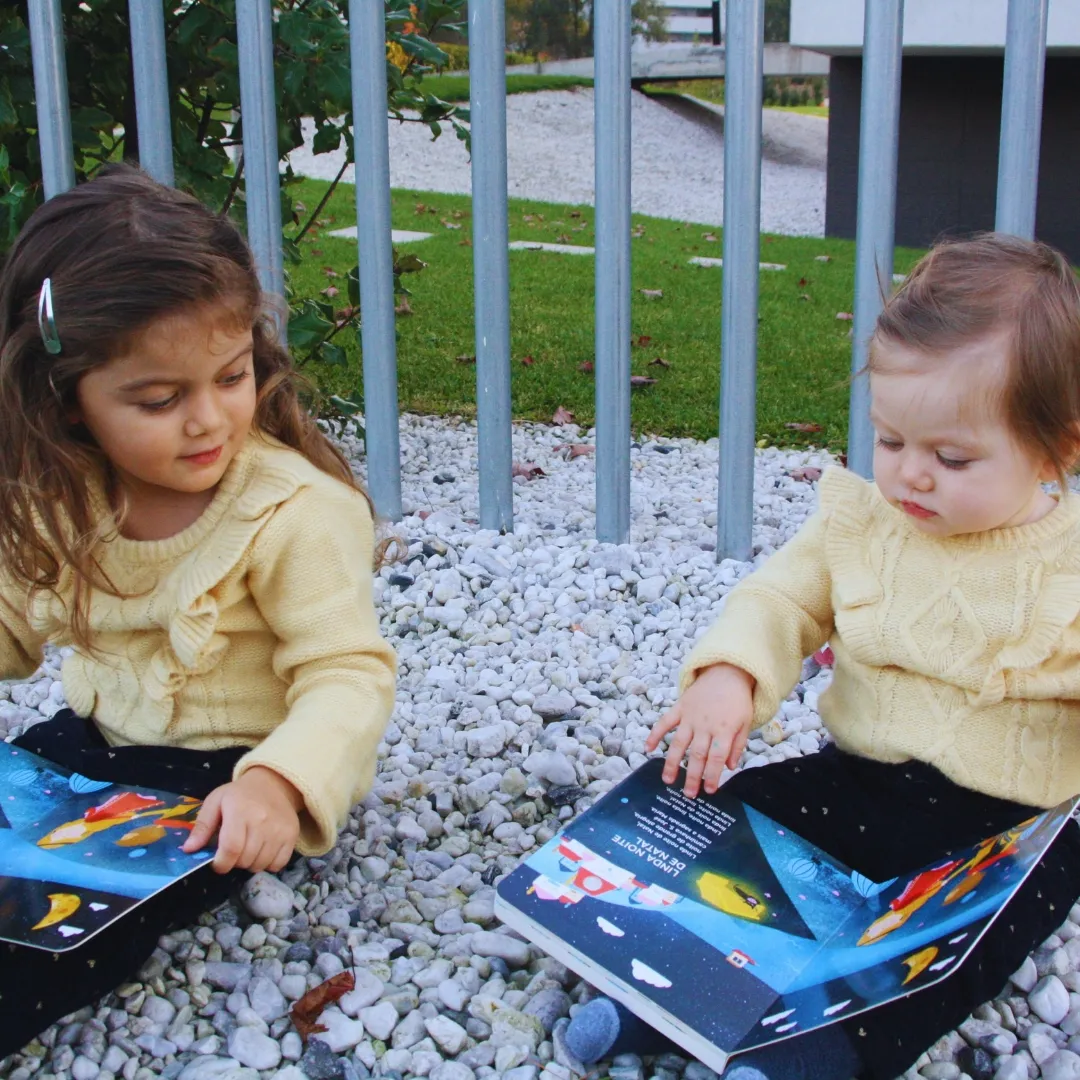 Duas crianças sentadas a ler livros infantis em pedras brancas ao ar livre