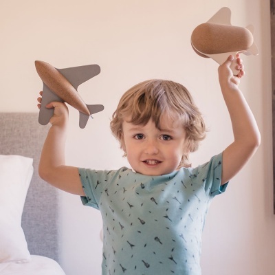 Criança segurando dois brinquedos de avião de madeira e cortiça no quarto