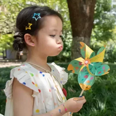 Menina com vestido branco e presilhas de estrela a soprar moinho de vento de papel colorido ao ar livre