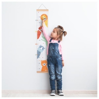 Menina a medir a sua altura num medidor de parede com desenhos de animais