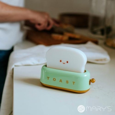 Torradeira decorativa verde com fatia de pão sorridente numa bancada branca
