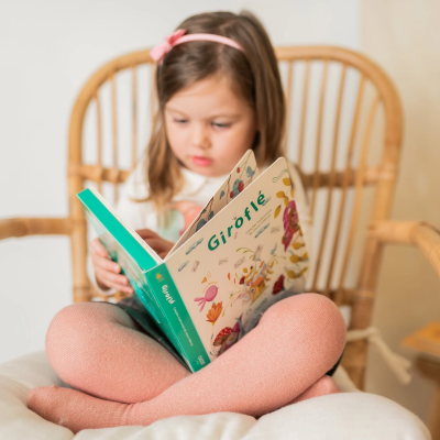 Menina com fita de cabelo rosa a ler livro infantil Giroflé sentada em cadeira de madeira clara