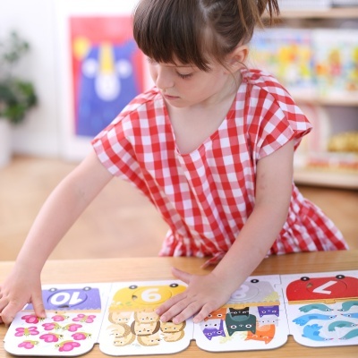 Menina em vestido xadrez vermelho branco a brincar com puzzle de madeira colorido com animais e números