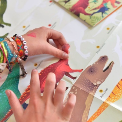 Mãos de criança a tocar figuras de dinossauros num jogo educativo colorido.